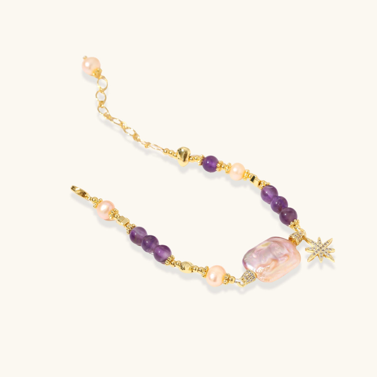 Gold-plated bracelet with baroque pearl centerpiece, amethyst beads, and crystal star charm on white background.