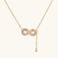 Gold infinity pendant with baguette crystals on adjustable chain against cream background.
