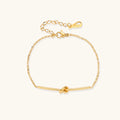 Delicate gold chain bracelet with minimalist bar and centered knot detail on cream background