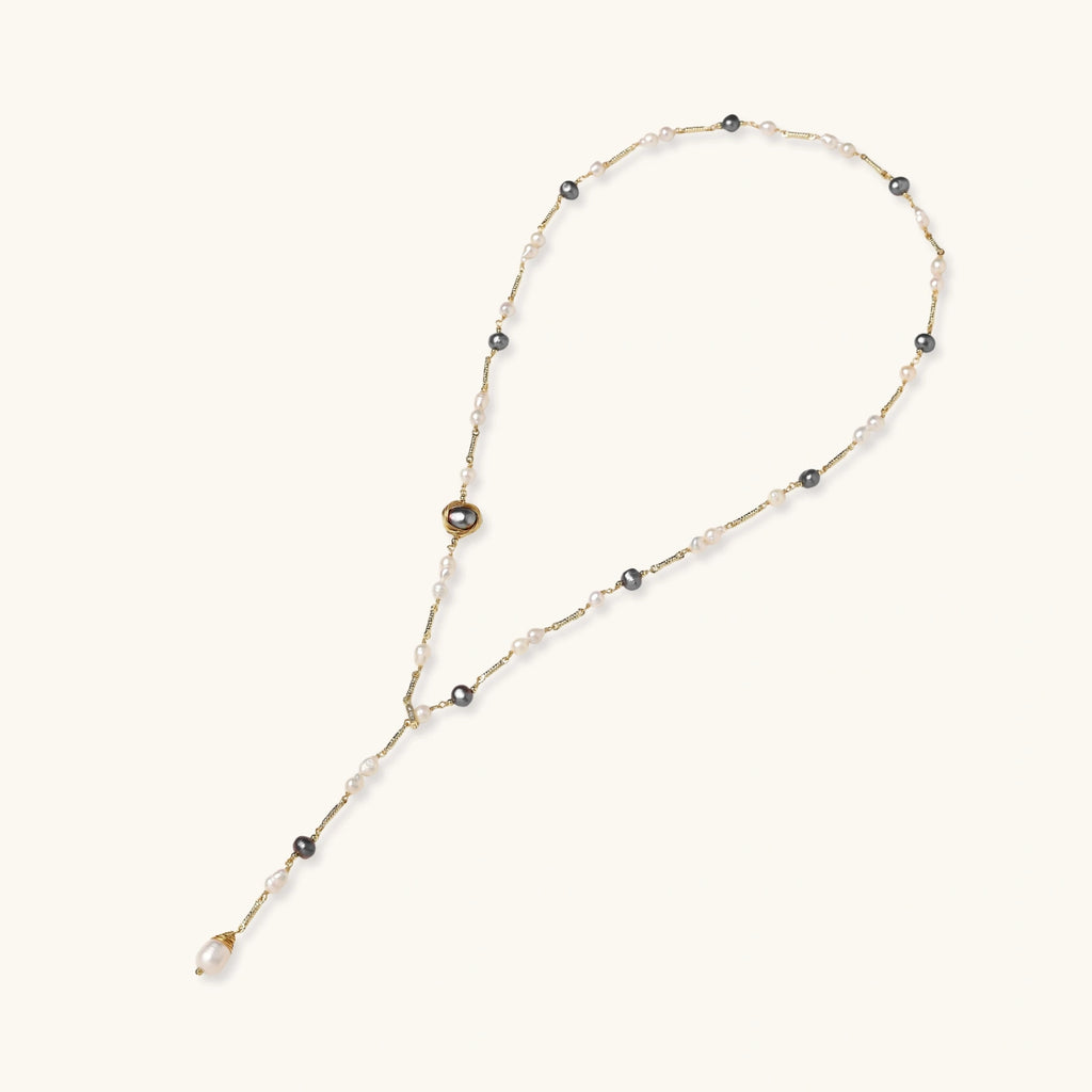 Y-shaped gold-plated necklace with white and gray freshwater pearls on cream background, showing adjustable drop design.